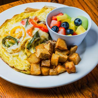 California omelet served alongside a bowl of mixed fruits and home fries.