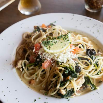 Tuscan Chicken pasta with spinach, black olives, grated cheese and a lemon garnish.