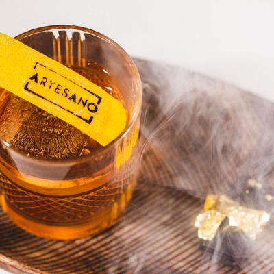 An Old Fashioned, served in a rocks glass on a wooden tray with smoke.