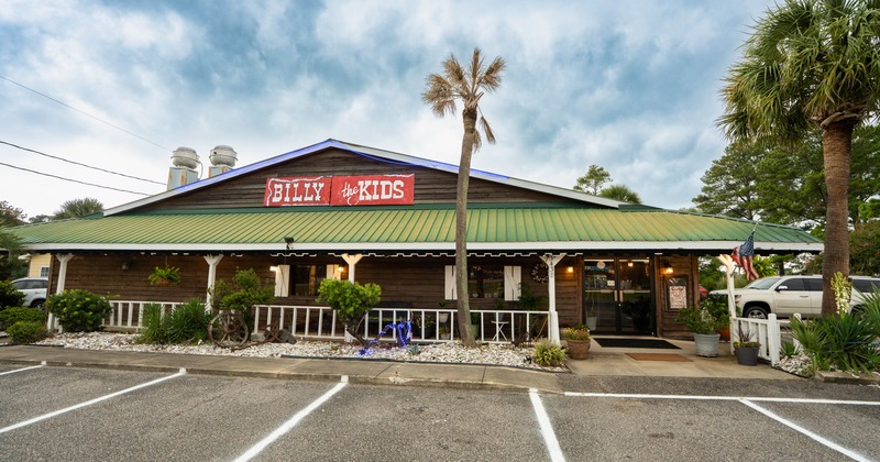 Exterior, wooden facade, a green roof, and a red sign, surrounded by palm trees and parked vehicles