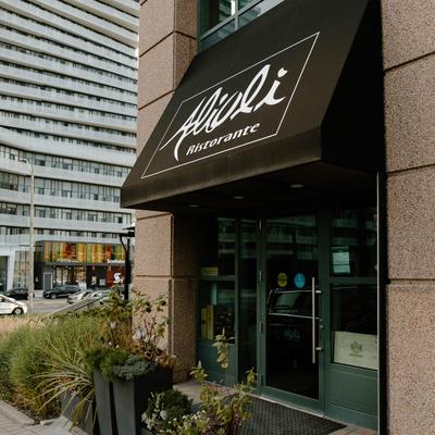 Exterior with a business name on black awning and potted plants.
