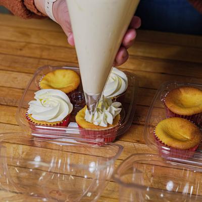 A hand decorating cupcakes with white icing using a pastry bag.