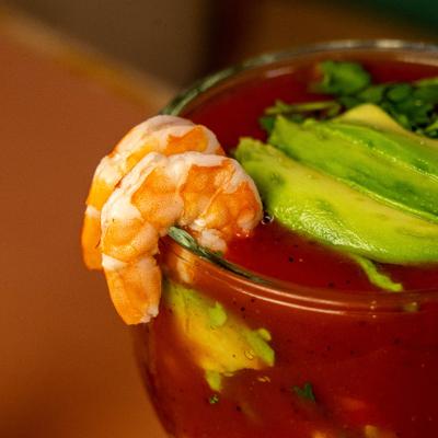 Shrimp cocktail served in a glass with sliced avocado and a tomato-based sauce.