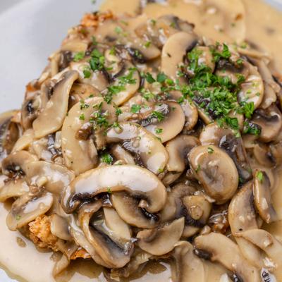 Fried chicken breast topped with creamy mushroom sauce and herbs.