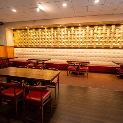 Dining area with warm lighting, a  textured wall panel, and a mix of booth and table seating.