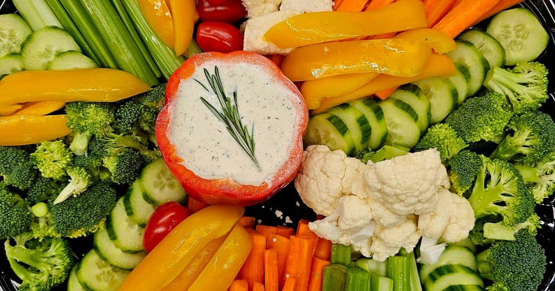 A platter of colorful fresh vegetables and a creamy dip in a red pepper