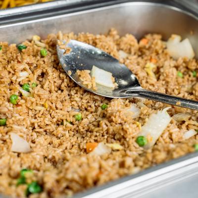 Fried rice with peas, carrots, and onions sits in a buffet tray.