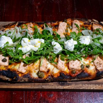 Pizza topped with salmon, capers, fresh arugula, and dollops of soft cheese.