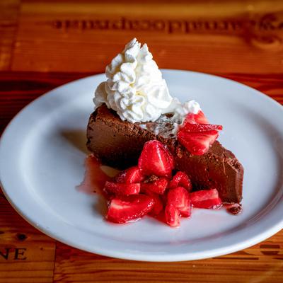 Chocolate cake slice topped with whipped cream and straberries.