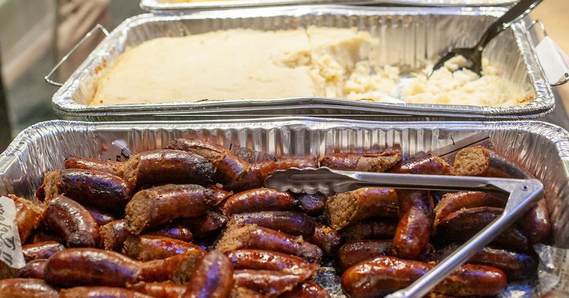 Lined up aluminium trays of grilled sausages, mashed potatoes and other dishes