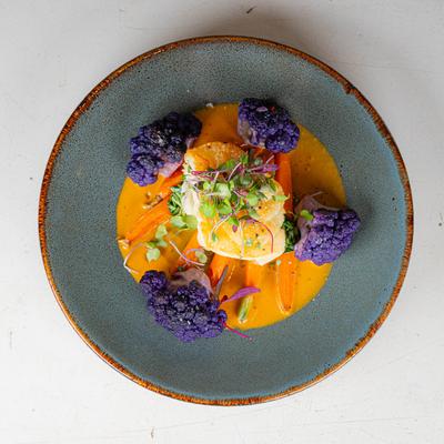 A dish of seared fish with microgreens, purple cauliflower, carrot slices in an orange sauce.