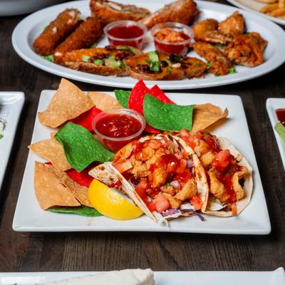 Fish tacos with salsa and colorful tortilla chips on a square plate.