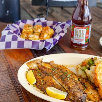 Plate of grilled fish fillet, alongside botthe of Iced Tea and basket of deviled eggs.