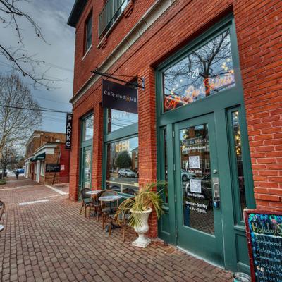 Brick wall exterior with entrance, signes and outdoor seating with small tables and chairs.