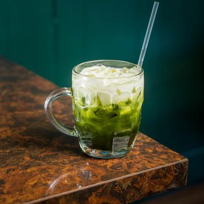 An iced matcha latte with milk in a glass mug on a counter.