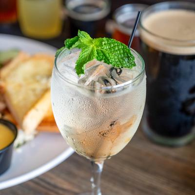 Clear cocktail in a wine glass, garnished with mint and served alongside a glass of beer.