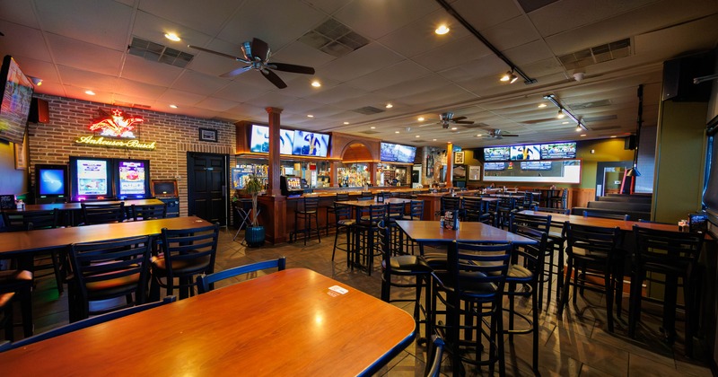Interior of a spacious bar with wooden tables, chairs, a long bar counter