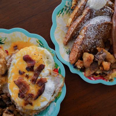 French toast with crispy smashed potatoes next to an egg sandwich with cheese and bacon.
