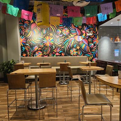 Restaurant interior with high seating, wall mural, and papel picado banners.