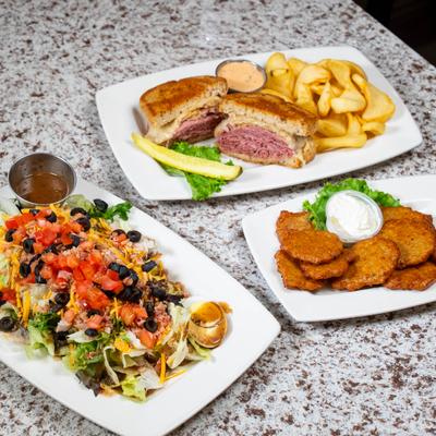Copper club salad with dressing, reuben sandwich with fries, and baby potato cakes.