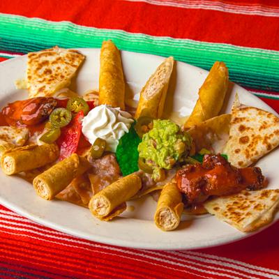 Mexican starter platter with taquitos, quesadilla pieces, jalapenos, guacamole, and sour cream.