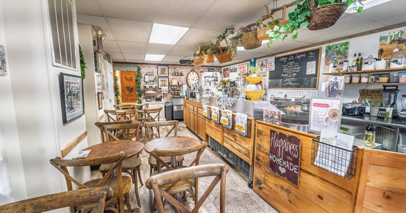 Cozy café with wooden tables, chairs and a rustic wooden counter with plants overhead.