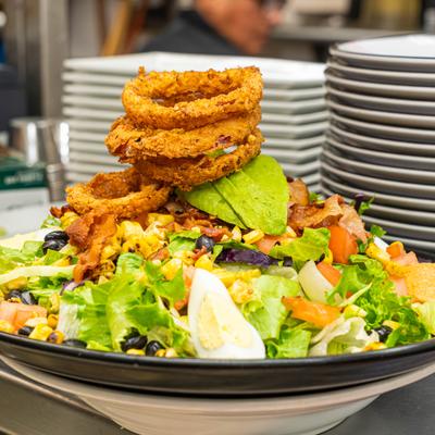 Large chopped salad topped with onion rings, avocado slices, bacon, corn, and boiled egg.