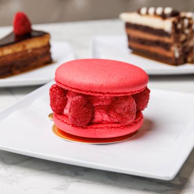 Raspberry macaroon with chocolate cakes in the background.
