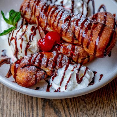 Twisted donuts topped with powdered sugar, chocolate drizzle, and whipped cream.