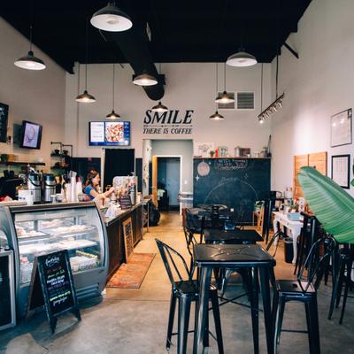 Interior with a counter with a display case, tables, chairs and plants.