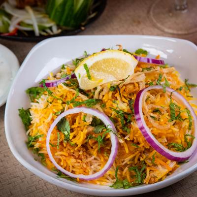 A bowl of chicken biryani rice garnished with red onion and lemon.
