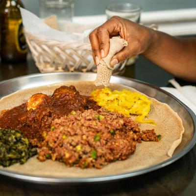 A person eating meat vegetable stews with sides, served over on top of traditional flatbread.