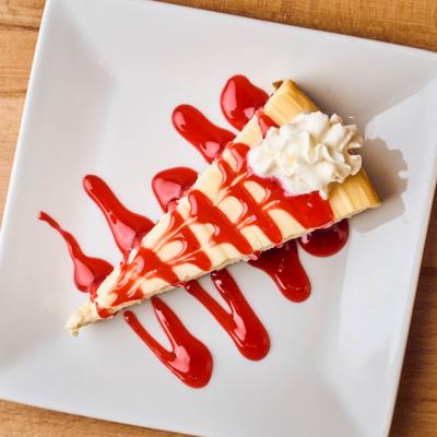 Cheesecake drizzled with strawberry sauce and topped with whipped cream.