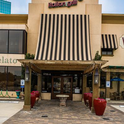 Restaurant exterior with partially visible signage, striped awning, and outdoor seating.