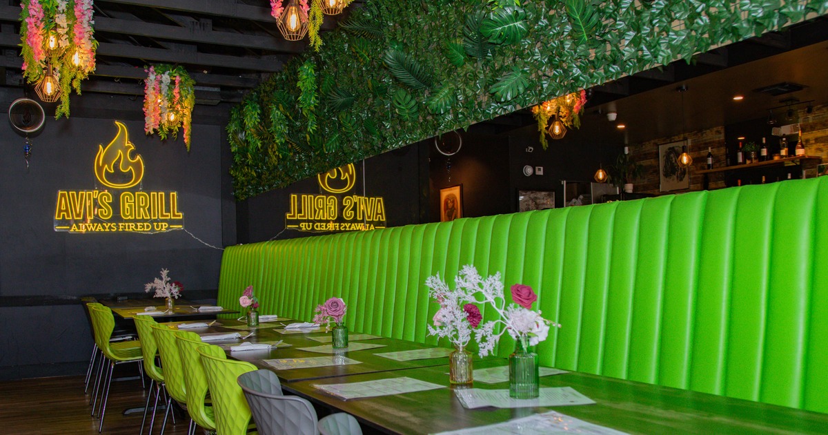 Interior of a restaurant with green booth seating, tables with flowers, and a neon sign