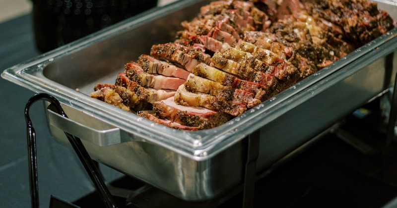 Sliced smoked brisket in a stainless steel catering dish