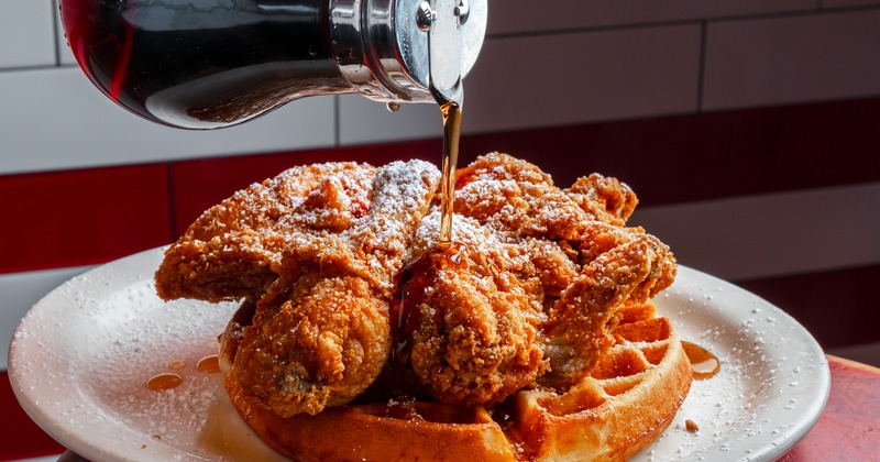 Chicken and waffles with powdered sugar being drizzled with syrup