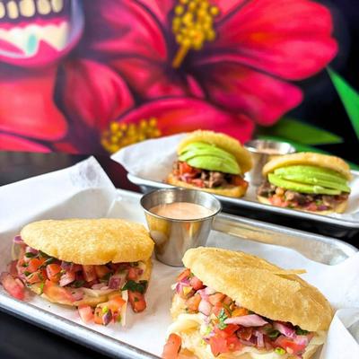 Two plates of different arepas served with dipping sauces.