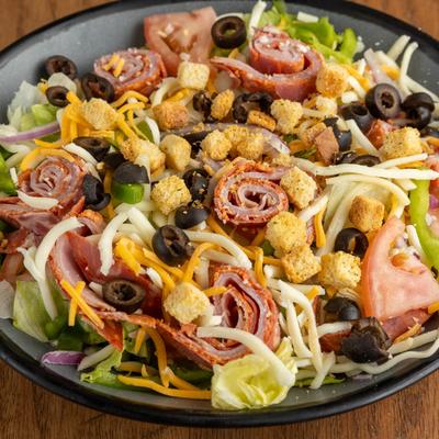 A colorful salad with rolled deli meats, shredded cheese, olives, and croutons.
