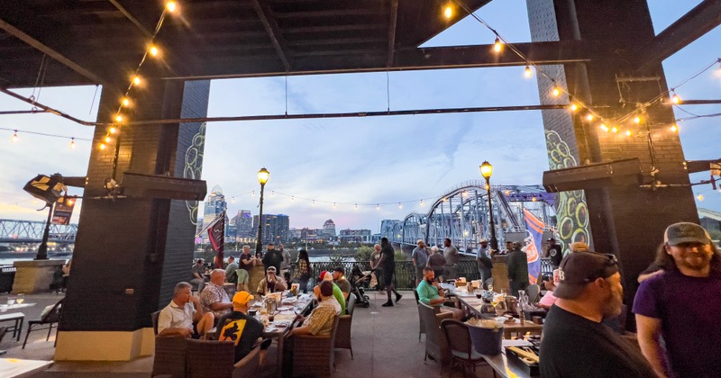 People sitting at tables outside with a bridge in the background