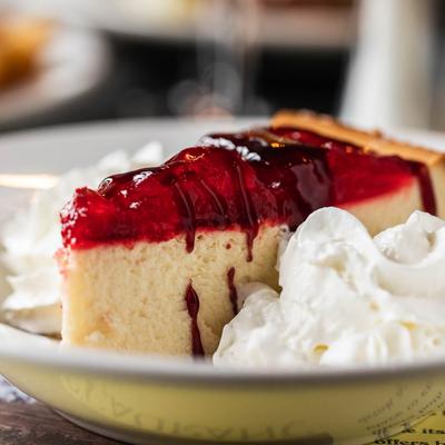 A slice of strawberry cheesecake with red berry topping and whipped cream on a plate.