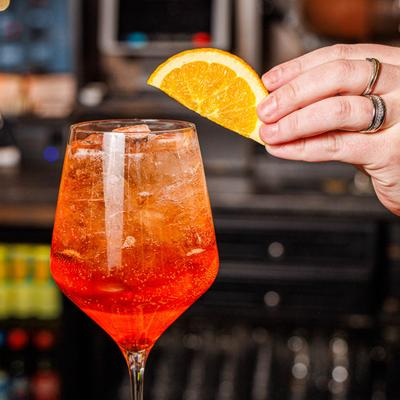 Hand garnishing an Aperol Spritz with an orange slice.