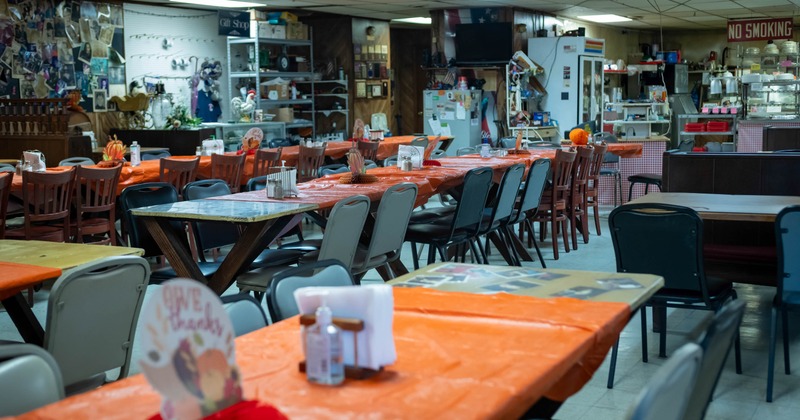 Interior of a rustic dining area with orange-covered tables, assorted chairs, and wall decorations