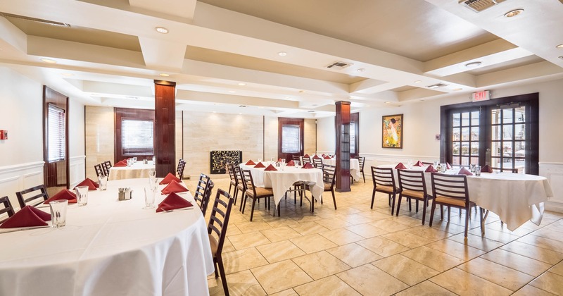 Elegant dining area with white tablecloths and red napkins, and a painting on the wall