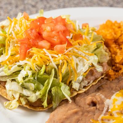 Tostada layered with refried beans, lettuce, shredded cheese, and diced tomatoes.