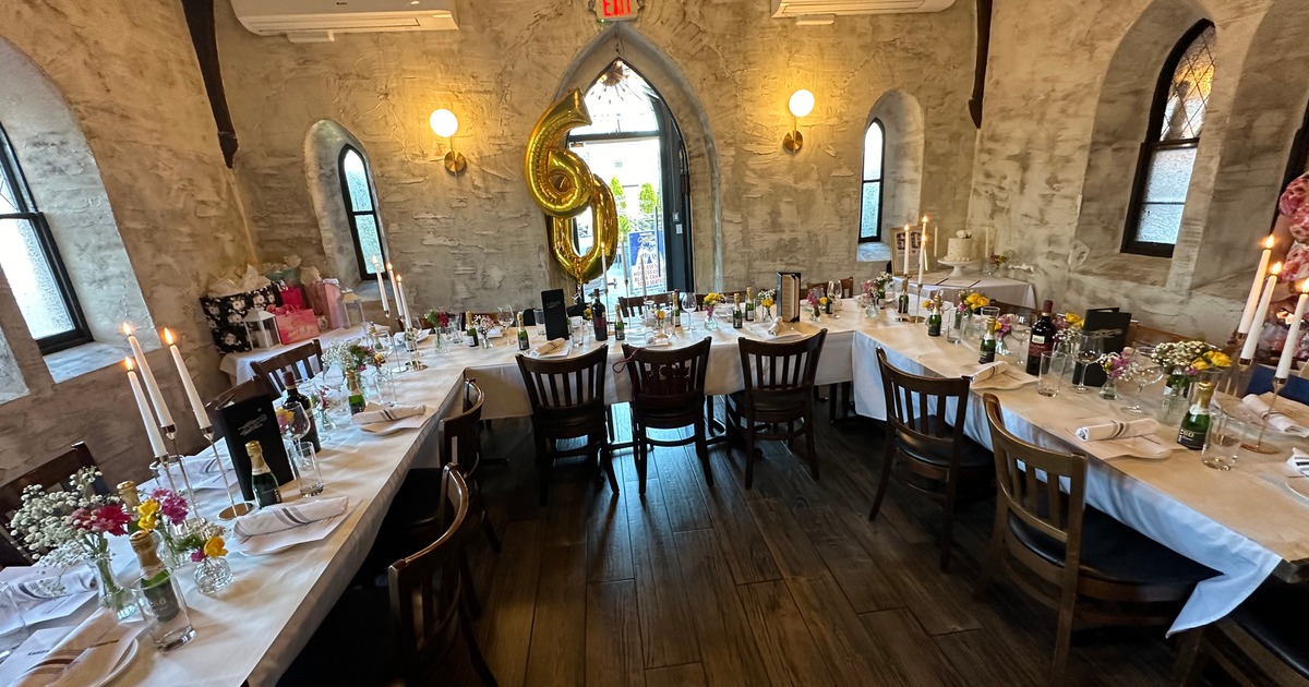 Dining room inside a stone building, long tables arranged and decorated for celebration