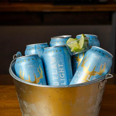 Metal bucket filled with blue cans of beer and lime wedges.