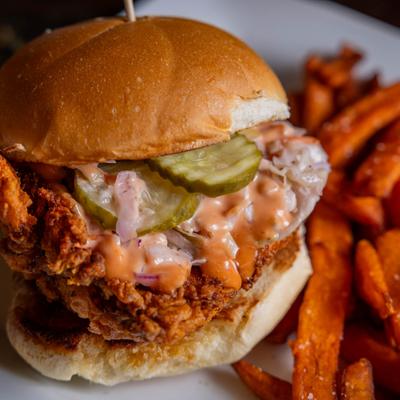 Fried chicken sandwich with coleslaw and pickles, served with sweet potato fries.