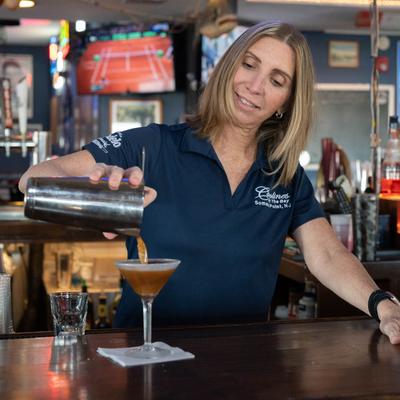 A bartender pouring a cocktail behind a bar counter.