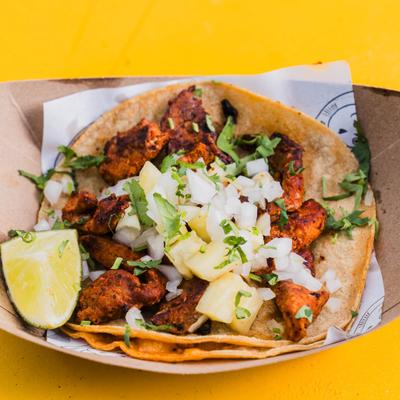 Taco Al Pastor topped with diced onion, cilantro, pineapple and a lime wedge.